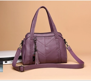 Detail of dark purple textured faux leather handbag with braided handle and tassel charm