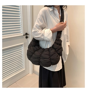 Detail of a black pleated dumpling bag worn by a model in a minimalist indoor setting