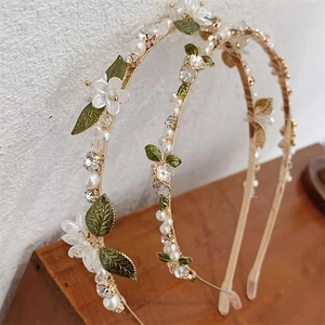Close-up of golden headband with white flowers, green leaves and crystal details