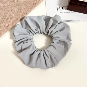 Detail shot of a grey oversized fabric scrunchie showing pleated texture on white background
