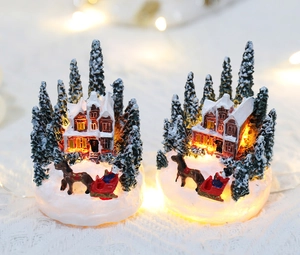 Macro shot of glowing resin Christmas house with snowy trees and warm interior lights