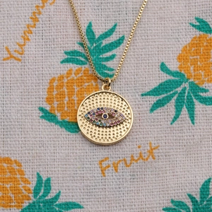 Close-up of golden evil eye pendant with colorful zircon stones on textured cloth