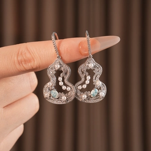 Detail of silver gourd earrings with blue gemstone and pearls held by a hand