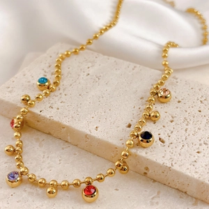 Gold beaded necklace with colorful round gemstone pendants on a beige stone surface