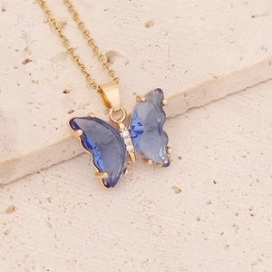 Close-up of gold butterfly pendant with blue glass wings on beige stone base