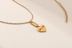 Detailed view of golden heart pendant with MOM engraving on polished metal necklace
