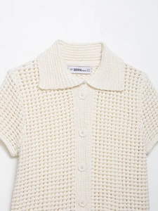 Détail du col polo en tricot crème et texture au crochet avec étiquette de taille