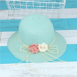 Détail d'un chapeau en paille vert menthe orné de fleurs en tissu rose et d'un nœud