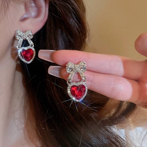 Detailed close-up of a silver bow earring with red heart gemstone worn on ear