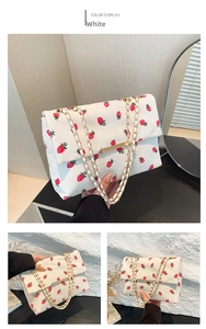 Detail of white corduroy shoulder bag with red strawberry print and gold chain strap