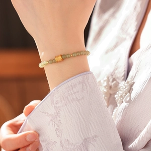 Detail of beaded jade bracelet with golden cylinder charm on a model's wrist