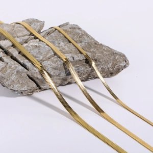 Flat gold snake bone chain necklaces in stainless steel draped over a grey stone