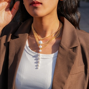 Detail of layered gold chain necklace featuring a vertical white faux pearl tassel charm
