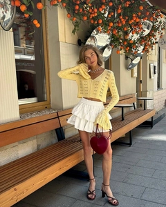 Detail of yellow knit cardigan with flared sleeves and white layered ruffle skirt