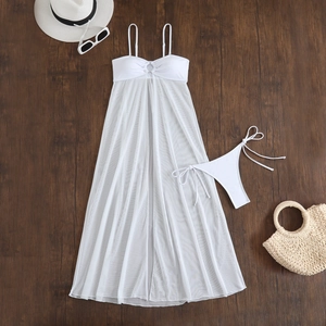 Three-piece white bikini set with mesh sarong and beach accessories on wood background