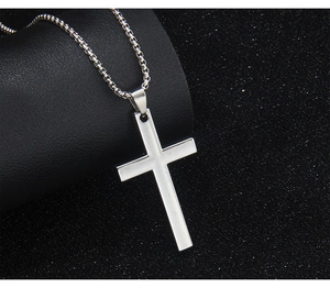 Close-up of polished silver stainless steel cross pendant on textured black background