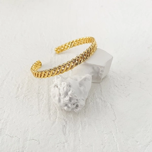 Detail of gold-plated open cuff bracelet with spiral woven design on a white pedestal