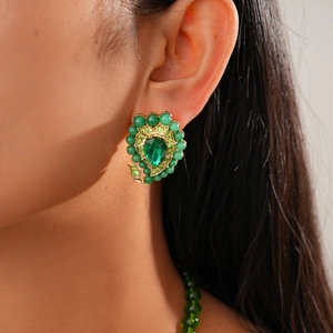 Close-up of vintage gold earrings with emerald green pear-cut crystals and beaded details