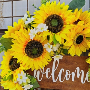 Détail de couronne de tournesols avec plaque de bienvenue en bois et fleurs jaunes