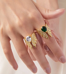 Close-up of golden angel wing rings with green and clear teardrop gemstones and micro-pave