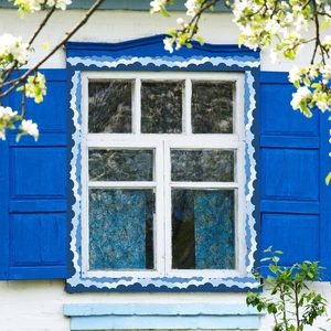Detailed view of floral stained glass window film on a white window with blue shutters