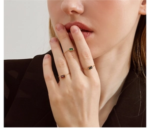 Close-up of thin gold chain rings with emerald green, ruby red, and black gemstones