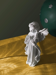 Detalle macro de figurita de ángel de resina blanca rezando sobre tela dorada