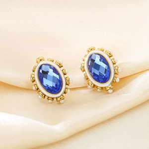 Macro detail of oval blue crystal earrings with white pearls on golden metal base