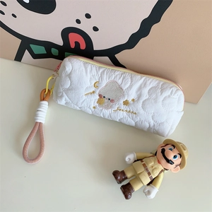 Close-up of white quilted pencil case featuring embroidered cartoon and braided handle