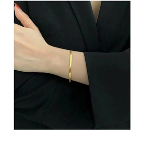 Close-up of minimalist gold flat snake bone bracelet worn on wrist with metal texture