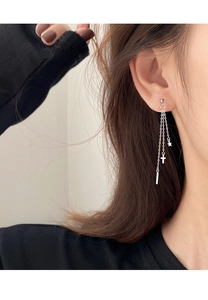 Detailed close-up of long silver tassel earrings with star and cross charms on model