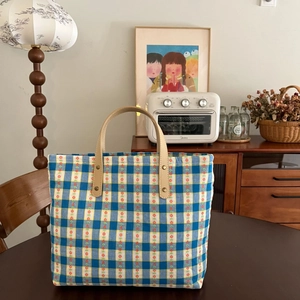 Macro detail of blue plaid canvas tote bag with floral patterns and leather handles