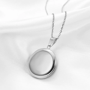 Detailed macro view of a round polished stainless steel locket necklace on white silk background