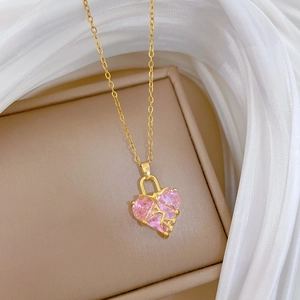 Gros plan du collier coeur rose avec cadre doré et lettre sur un écrin beige