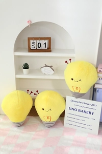 Detailed view of yellow plush light bulb pillows with heart antennas on a cozy shelf