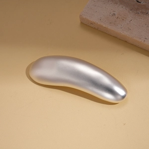 Macro detail of a minimalist silver metallic bean-shaped brooch on beige leather texture