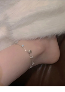 Close-up of a silver zircon flower anklet on a model ankle with a luxury background