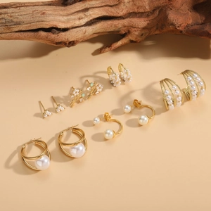 Detailed view of six pairs of elegant gold pearl earrings on a warm beige background