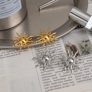 Macro detail of sunburst stud earrings in gold and silver finish on metallic tray