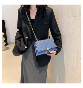 Close-up of blue denim quilted chain bag with gold square lock on a model in a black suit