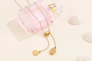 Golden heart pendant necklace with y-shaped chain and embossed coins over a pink perfume bottle