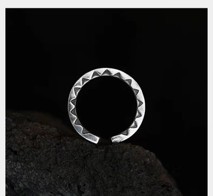 Detailed view of silver ring with geometric triangle patterns on black volcanic rock