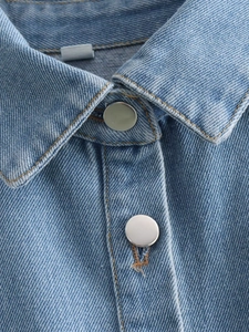 Détail de la texture du denim bleu clair et bouton en métal argenté sur le col polo