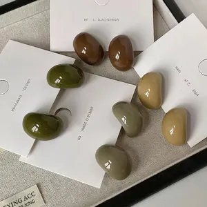 Minimalist C-shaped resin stud earrings in earthy tones displayed on display card
