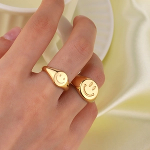 Polished gold smiley face signet rings on fingers against a silk fabric background
