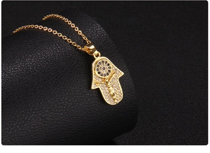 Detailed close-up of gold-plated Hamsa pendant with zircon stones on a dark background