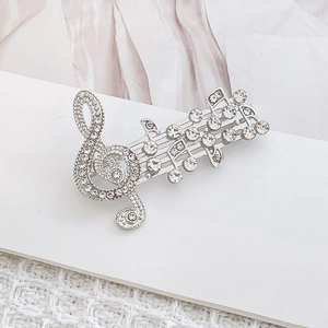 Elegante spilla a nota musicale argentata con strass scintillanti su tessuto bianco