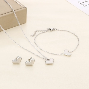 Flat lay of silver heart jewelry set including necklace, bracelet and stud earrings