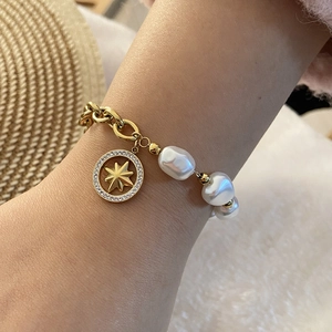 Detail view of gold chain bracelet with pearls and octagonal star charm on wrist