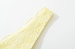 Dettaglio del tessuto in cotone giallo tenue con delicato ricamo floreale traforato